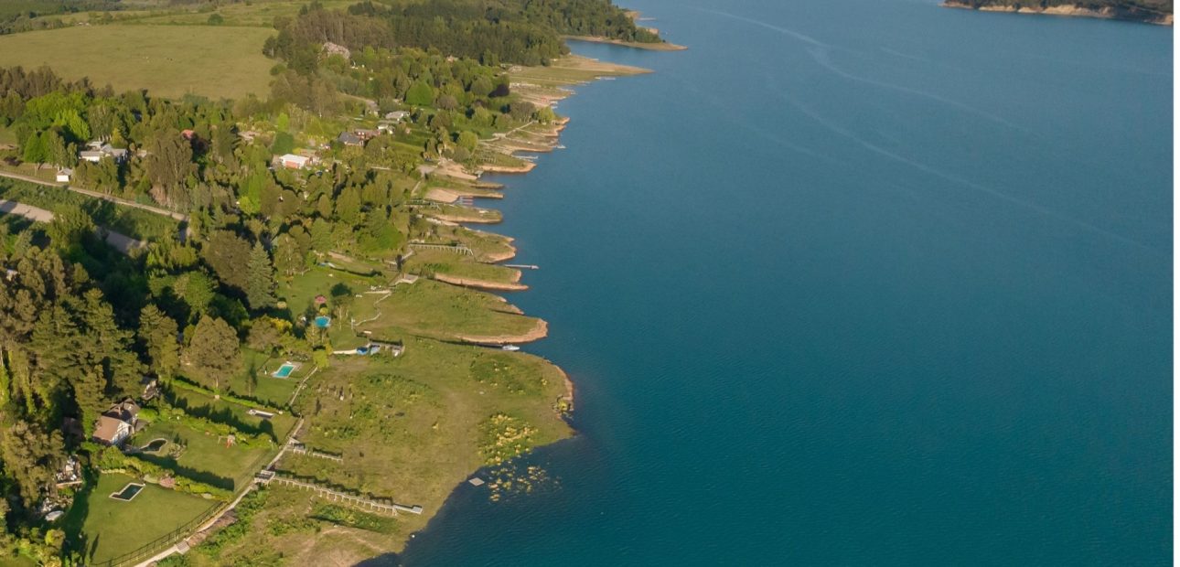 Orilla de la ribera norte del Lago Colbún vista desde el aire, con el agua llegando a cada bahía
